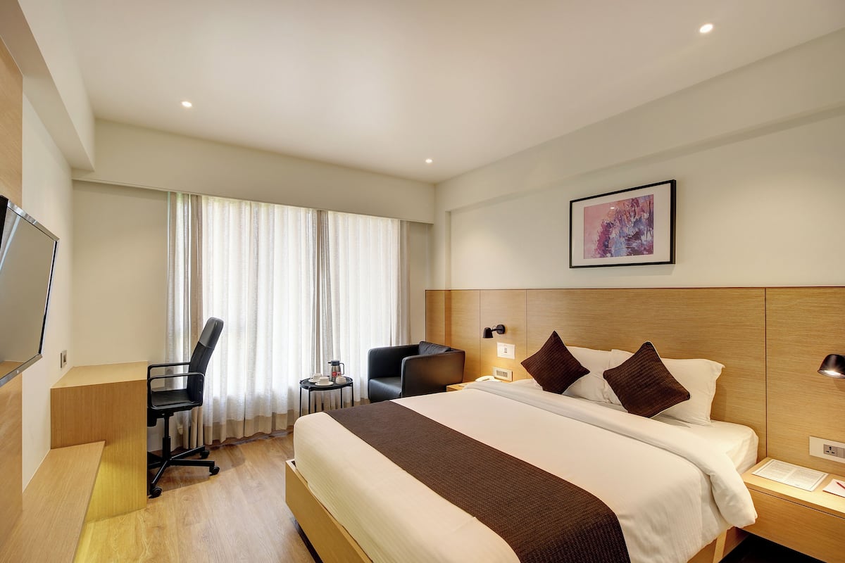 Habitación de hotel con cama, escritorio, silla, una mesita de noche con lámpara y un cuadro en la pared.