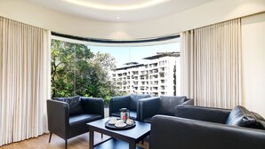 Una sala de estar moderna con un juego de sofá, una mesa de centro y vistas a un edificio y árboles a través de amplios ventanales.