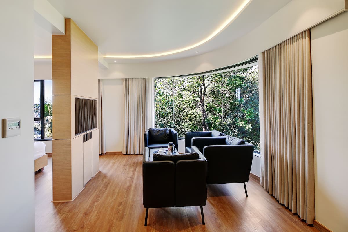 Una sala de estar moderna con sofá, una mesa de centro y televisor. Hay un ventanal con cortinas y suelo de madera.