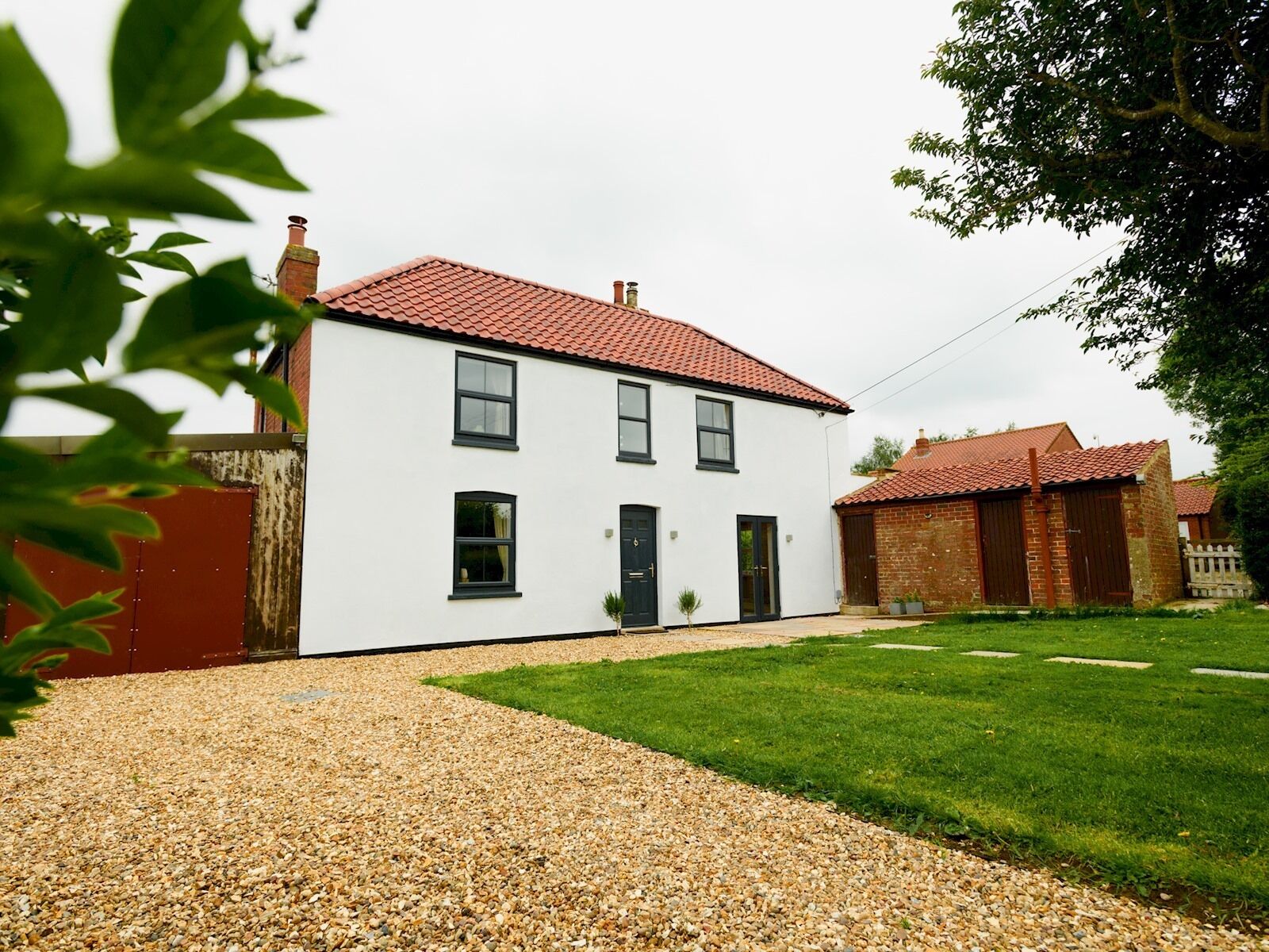 A two-story white house with a red-tiled roof, a gravel driveway, and a well-maintained lawn.