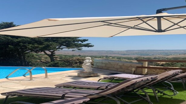 A poolside area with lounge chairs, a stone wall, and a view of the landscape.