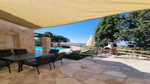 An outdoor patio with stone flooring, a table with chairs, and a covered area with a view of the landscape.