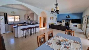 A spacious kitchen with an island, a dining area with a table and chairs, and a living area with a sofa and TV.