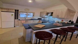 A kitchen with a central island, bar stools, a microwave, and a clock on the wall.