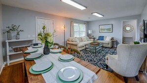 Un coin repas avec une table en bois dressée pour quatre personnes, un canapé et un tapis à motifs.