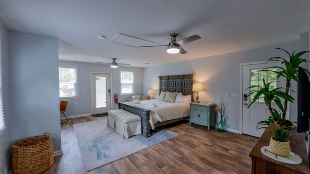Une chambre à coucher avec un grand lit, un ventilateur de plafond, une table de chevet, une commode et une fenêtre.