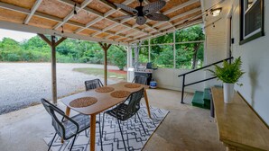 Une terrasse couverte avec une table et des chaises, un ventilateur de plafond et un barbecue.