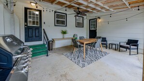 Un espace extérieur abrité comprenant un barbecue, une table à manger, des chaises et un ventilateur de plafond.