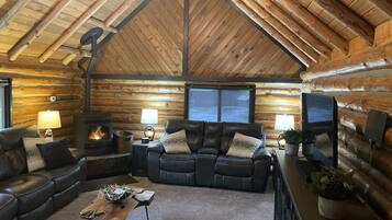 L’intérieur d’une cabane en rondins, avec une cheminée, des canapés en cuir, un téléviseur et une atmosphère chaleureuse.