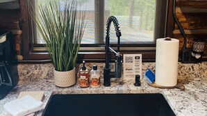 A kitchen with a granite countertop, a black sink, a potted plant, and a window with a view of trees. - Little Cabin in the Woods + Disk - Frisbee Golf (Post Falls)