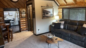 A cabin interior with a wooden ceiling, a dining area, a living room with a leather couch, and a rustic wall decor. - Little Cabin in the Woods + Disk - Frisbee Golf (Post Falls)