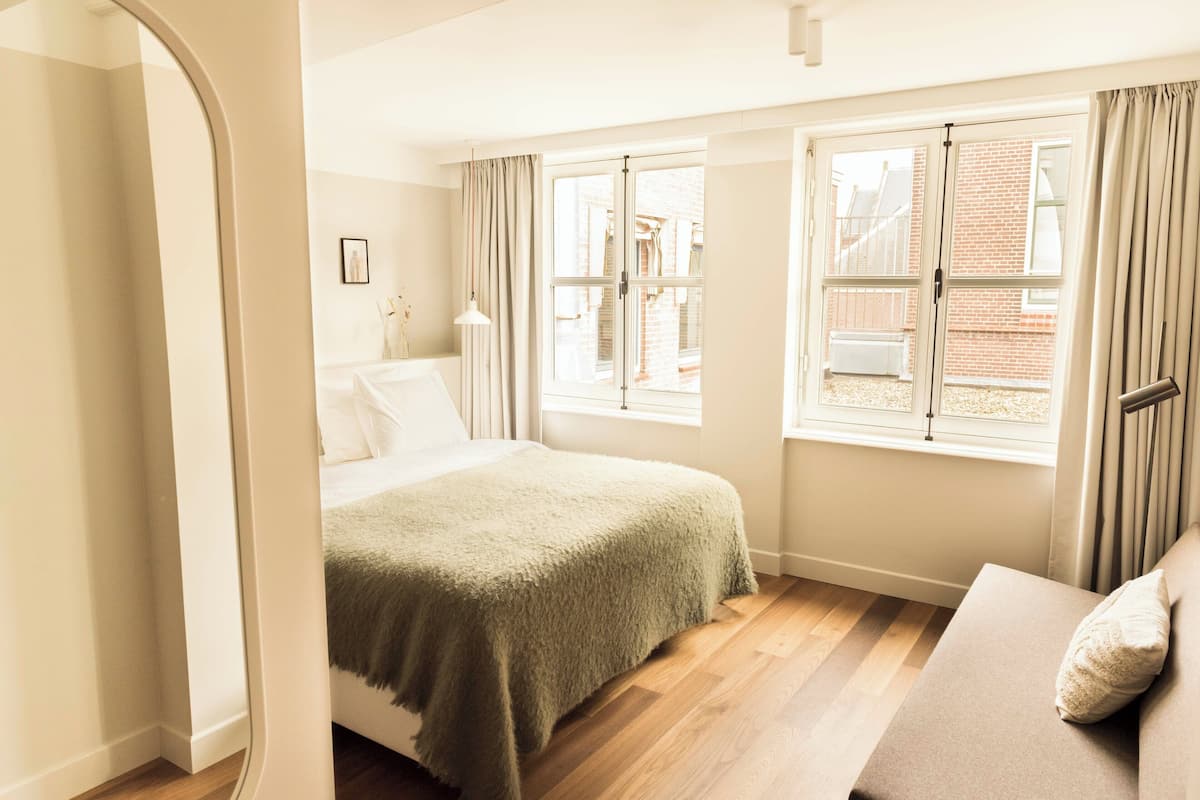 A bedroom with a bed, a sofa, and two windows with curtains.