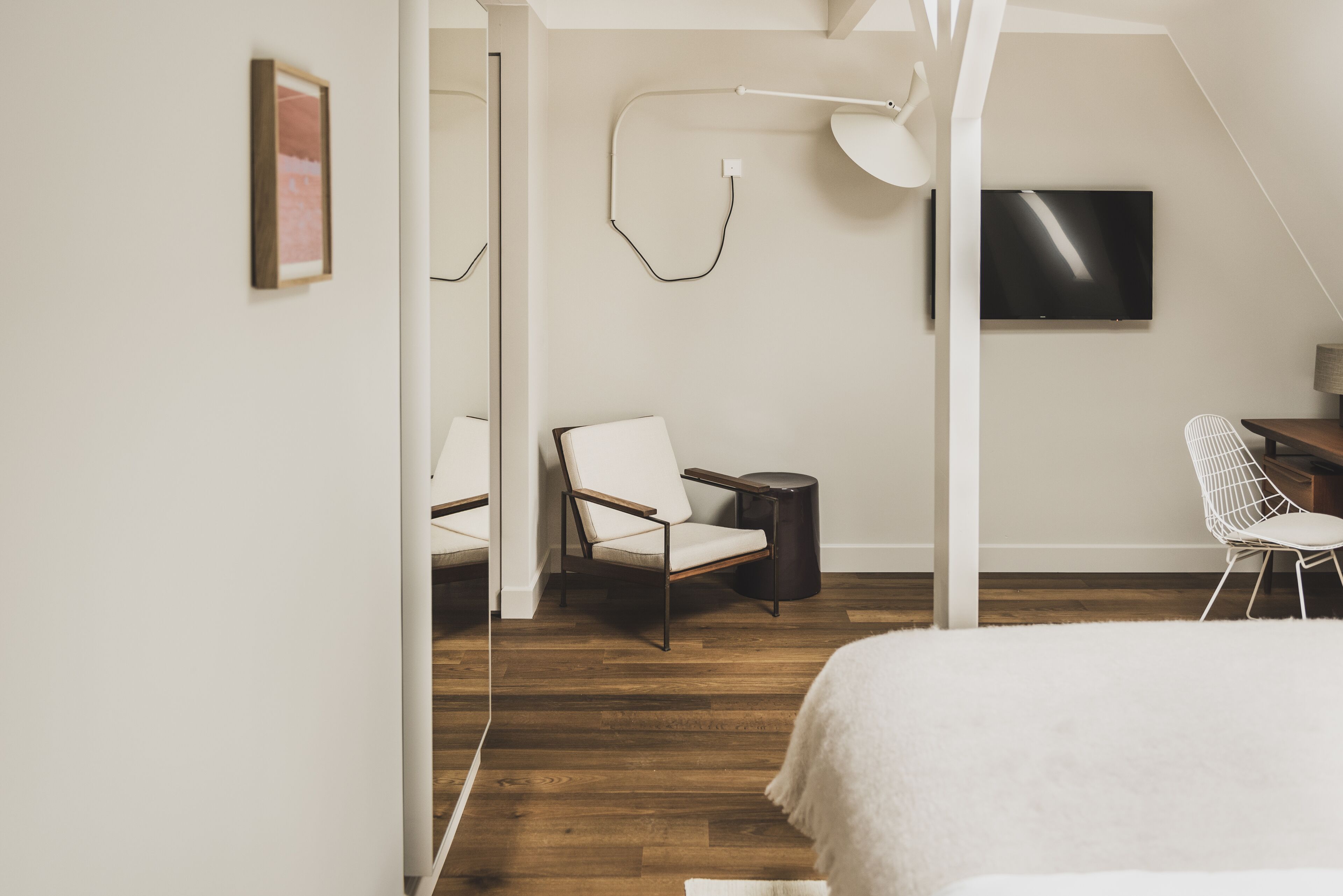 A bedroom with a bed, a chair, a desk, a TV, and a lamp.