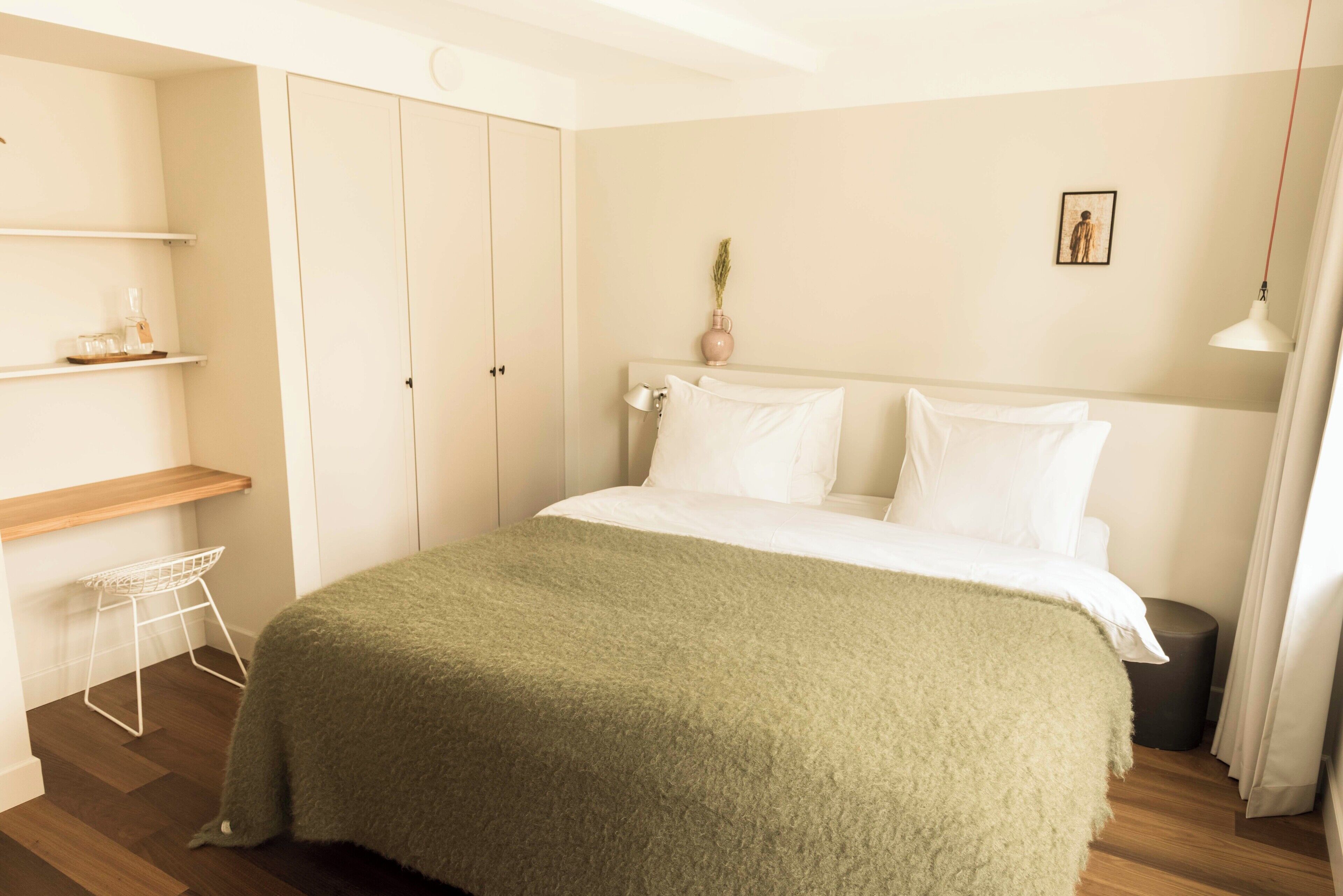 A bedroom with a bed, a bedside table, a shelf with a vase, and a wardrobe.