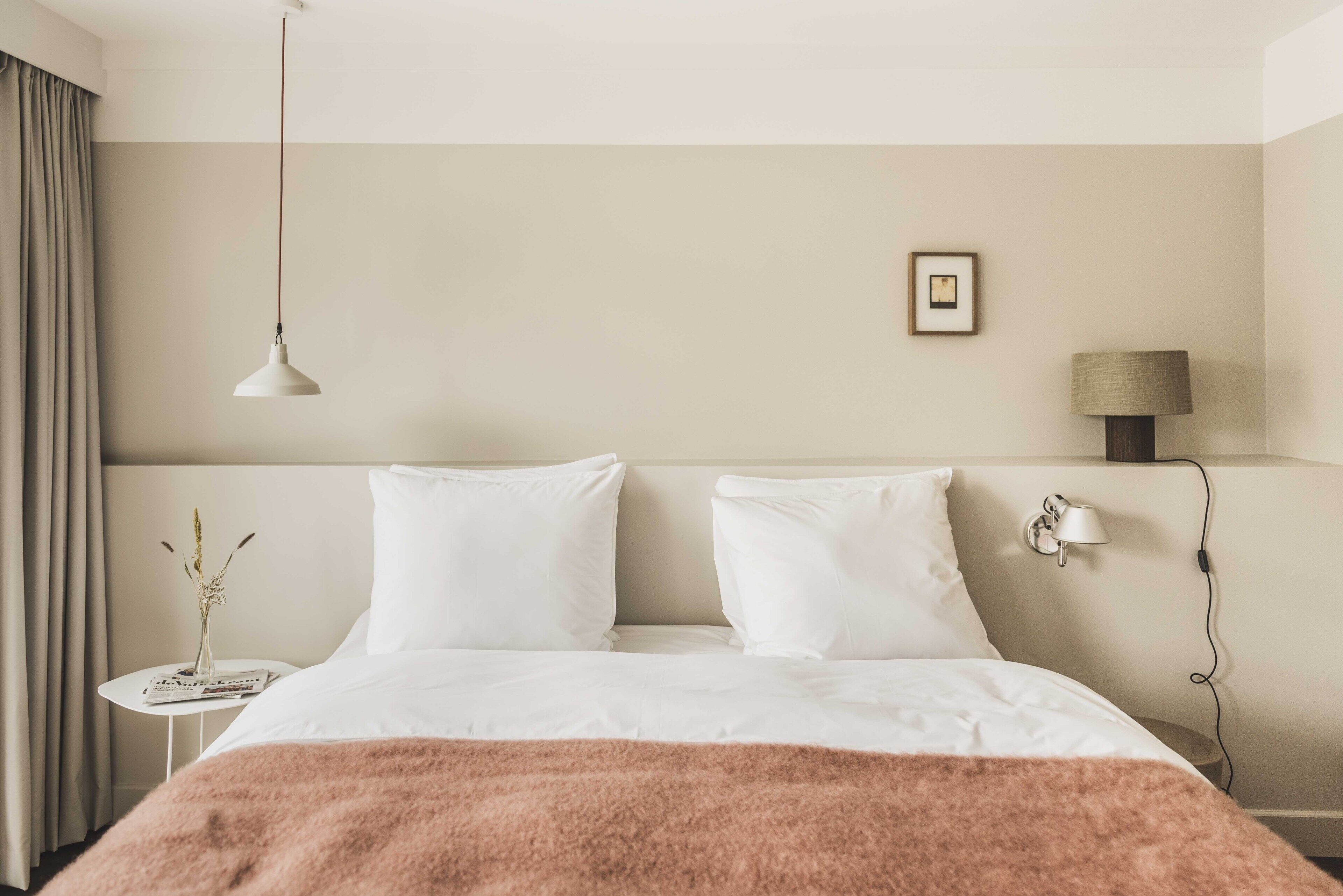 Een hotelkamer met een bed, nachtkastje, lamp en een schilderij aan de muur.