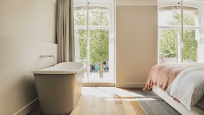 A modern bathroom with a bathtub, large windows, and a view of greenery outside. - Boutique Hotel Weesp (Weesp)
