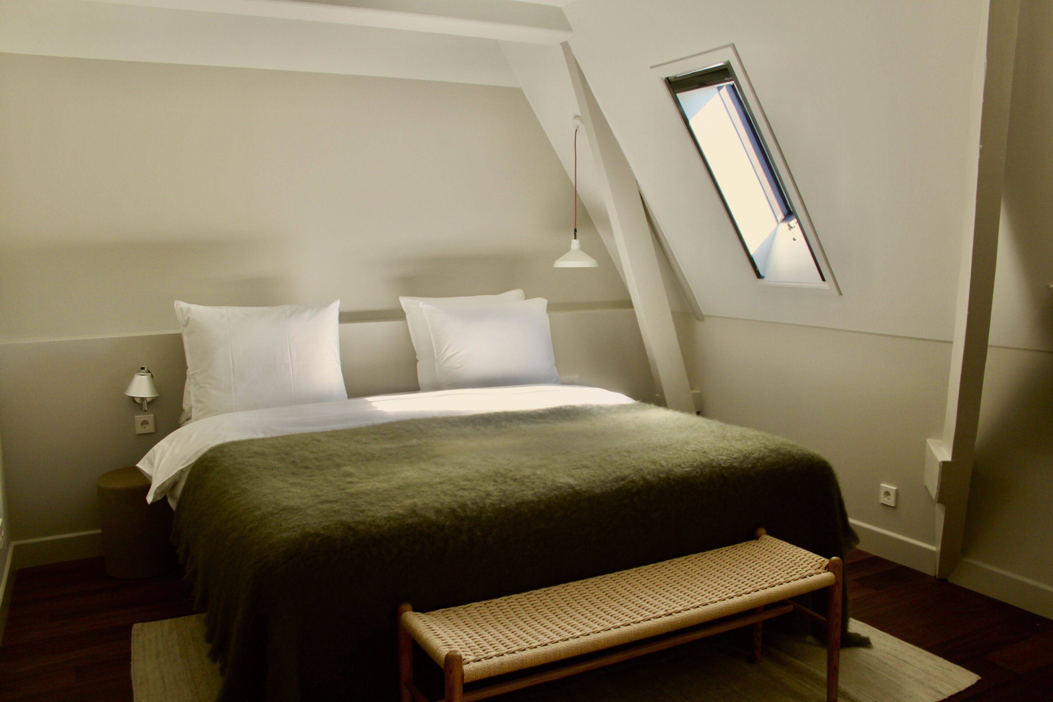 Ein Schlafzimmer mit einem Bett, einer Bank, einer Lampe und einem Dachfenster.