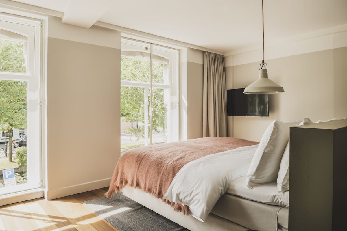A bedroom with a bed, a TV mounted on the wall, and a large window with curtains.