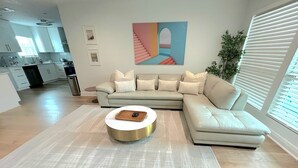 A modern living room with a sectional sofa, a round coffee table, and a large abstract painting on the wall. - Culdesac Heights Cottage with Enclosed Parking (Houston)