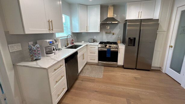 A modern kitchen with white cabinets, stainless steel appliances, and a wooden floor. - Culdesac Heights Cottage with Enclosed Parking (Houston)