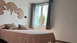 Une chambre à coucher avec un lit, des oreillers, un ventilateur fixé au mur et une fenêtre avec des rideaux.