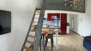Un espace de vie compact avec un escalier menant à une cuisine, une table à manger et un canapé bleu.