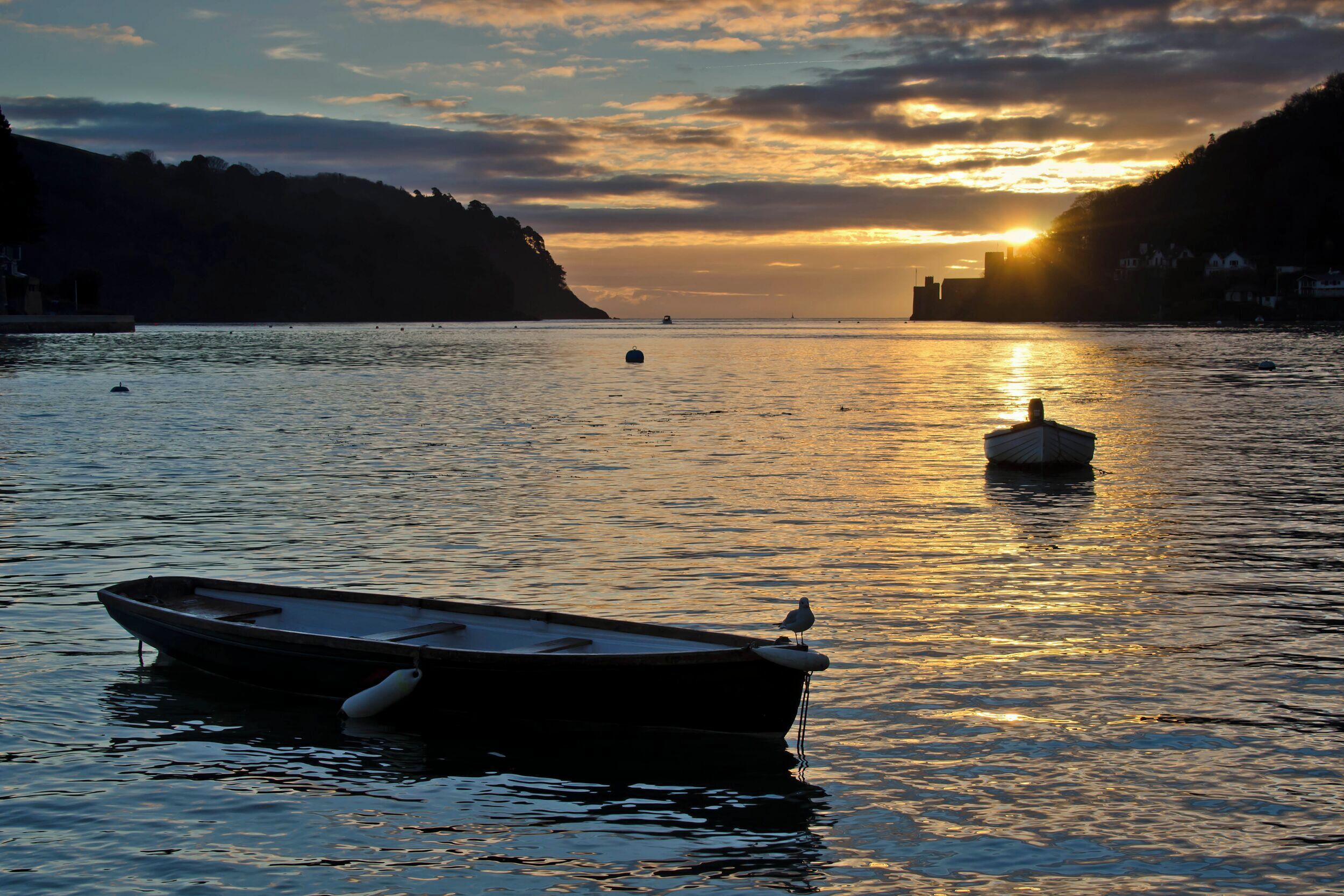 Un bote anclado cerca de la orilla con un atardecer de fondo.