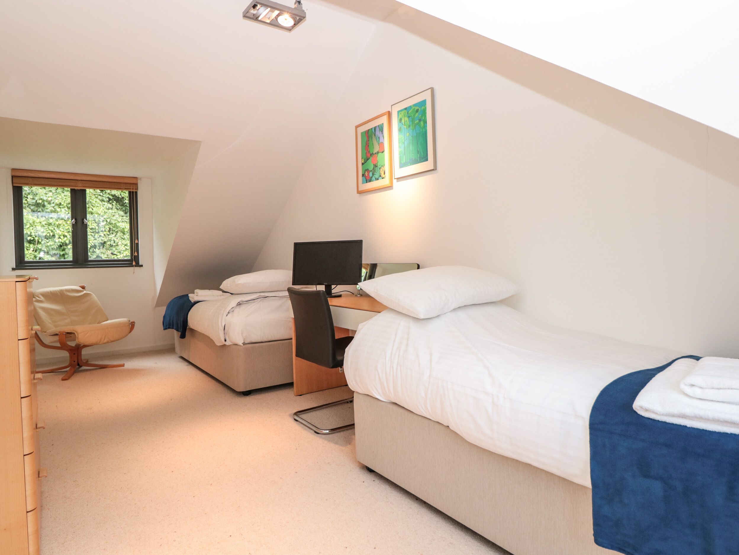 Een slaapkamer met een bed, een bureau met een computer, een stoel en een raam.