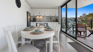A modern kitchen with white cabinets and a dining area with a round table and white chairs. - Husky Sol Coastal escape, walk to beach and cafes (Huskisson)