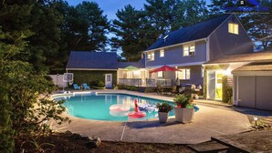 A backyard with a swimming pool, a patio with outdoor furniture, and a house with a covered porch.
