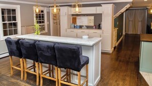 A modern kitchen with a central island, bar stools, pendant lighting, and a view of the dining area.