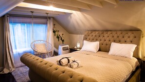 A bedroom with a large bed, a hanging chair, a nightstand, and a lamp.