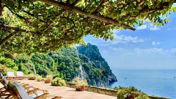 Una terraza con sillones de madera y vistas al mar y un acantilado.