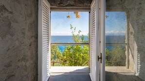 Un umbral abierto que da a un balcón con vista al mar y la vegetación.