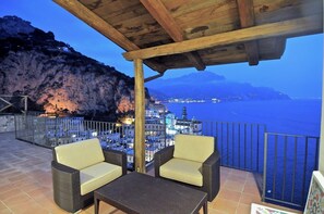 A terrace with wicker furniture and a view of a coastal city at dusk. - VILLA AMALFI - Twelve Bedroom Villa, Sleeps 24 (Amalfi)
