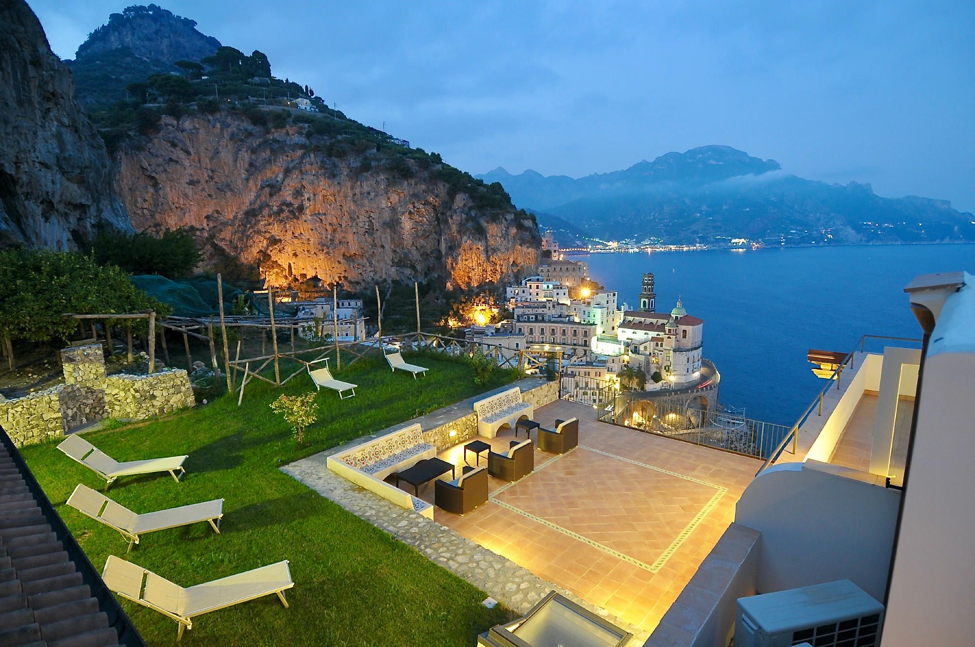 Une propriété située sur la côte, dotée d’une terrasse, de chaises longues et offrant une vue sur la mer et les montagnes.