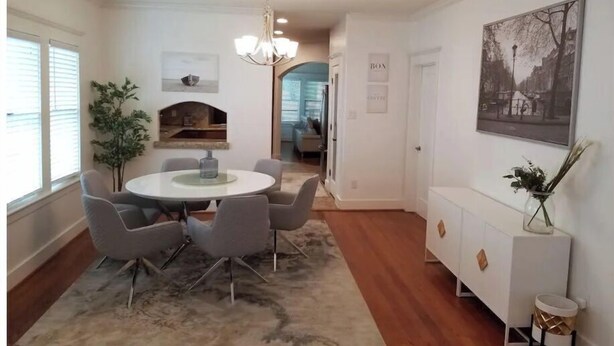 A dining area with a round table, grey chairs, a chandelier, a fireplace, and a view into another room. - Lovely Heights Cottage 🌅🌄 (Fenced Yard, Garage) (Houston)