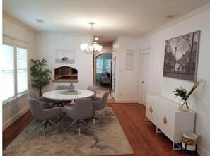 A dining area with a round table, grey chairs, a chandelier, a fireplace, and a view into another room. - Lovely Heights Cottage 🌅🌄 (Fenced Yard, Garage) (Houston)