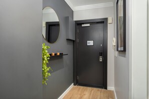 A hallway with a dark door, a wall-mounted mirror, a small plant, and a thermostat.
