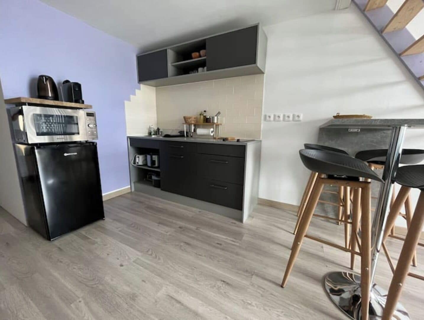 Une cuisine compacte équipée d’un four à micro-ondes encastré, d’un réfrigérateur et d’un tabouret de bar.