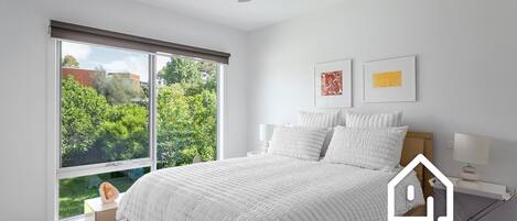 A bedroom with a large window, a bed, a ceiling fan, and two wall-mounted lamps.