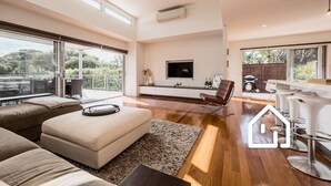 A spacious living room with a large window, a flat-screen TV, a brown leather chair, and a bar area. - The Cosmopolitan *1 NIGHT FREE* Stay in the Heart of Sorrento (Sorrento)