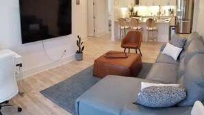 Moderni olohuone, jossa on taulutelevisio, sohva, sohvapöytä ja ruokailutila tuoleineen.