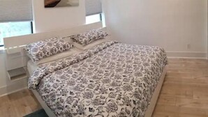 Makuuhuone, jossa on sänky, kaksi ikkunaa, peili ja puulattia.