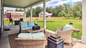Eine überdachte Terrasse mit Korbmöbeln, einem Grill und Blick auf ein Bauernhaus und ein Wohnhaus in ländlicher Umgebung.