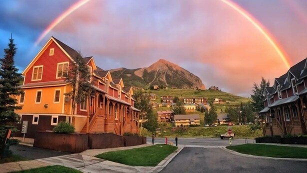 Un barrio residencial con una montaña destacada al fondo y un arcoíris cruzando el cielo.