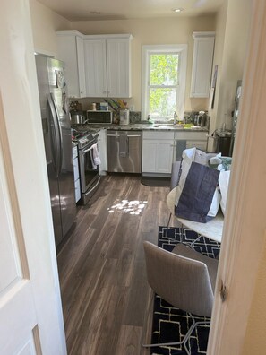 A modern kitchen with white cabinets, stainless steel appliances, and a window providing natural light.