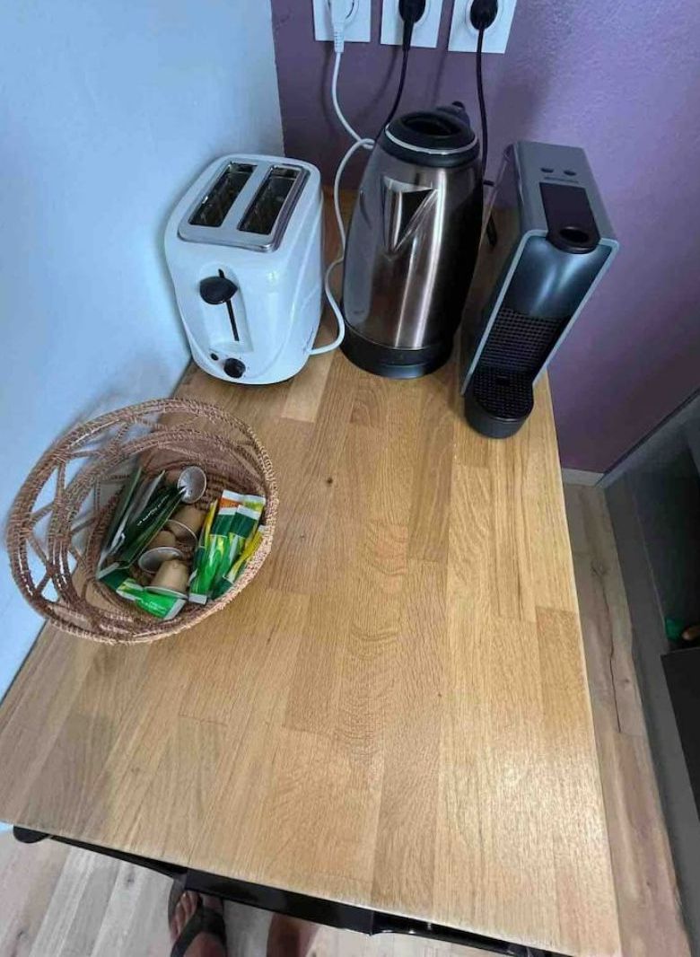 A kitchen counter with a toaster, a kettle, a portable heater, and a basket of snacks.