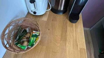A kitchen counter with a toaster, a kettle, a portable heater, and a basket of snacks.