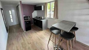 Une cuisine compacte équipée d’un four à micro-ondes, d’un évier et d’un petit plan de travail. Un coin repas avec une table et deux chaises est également disponible.